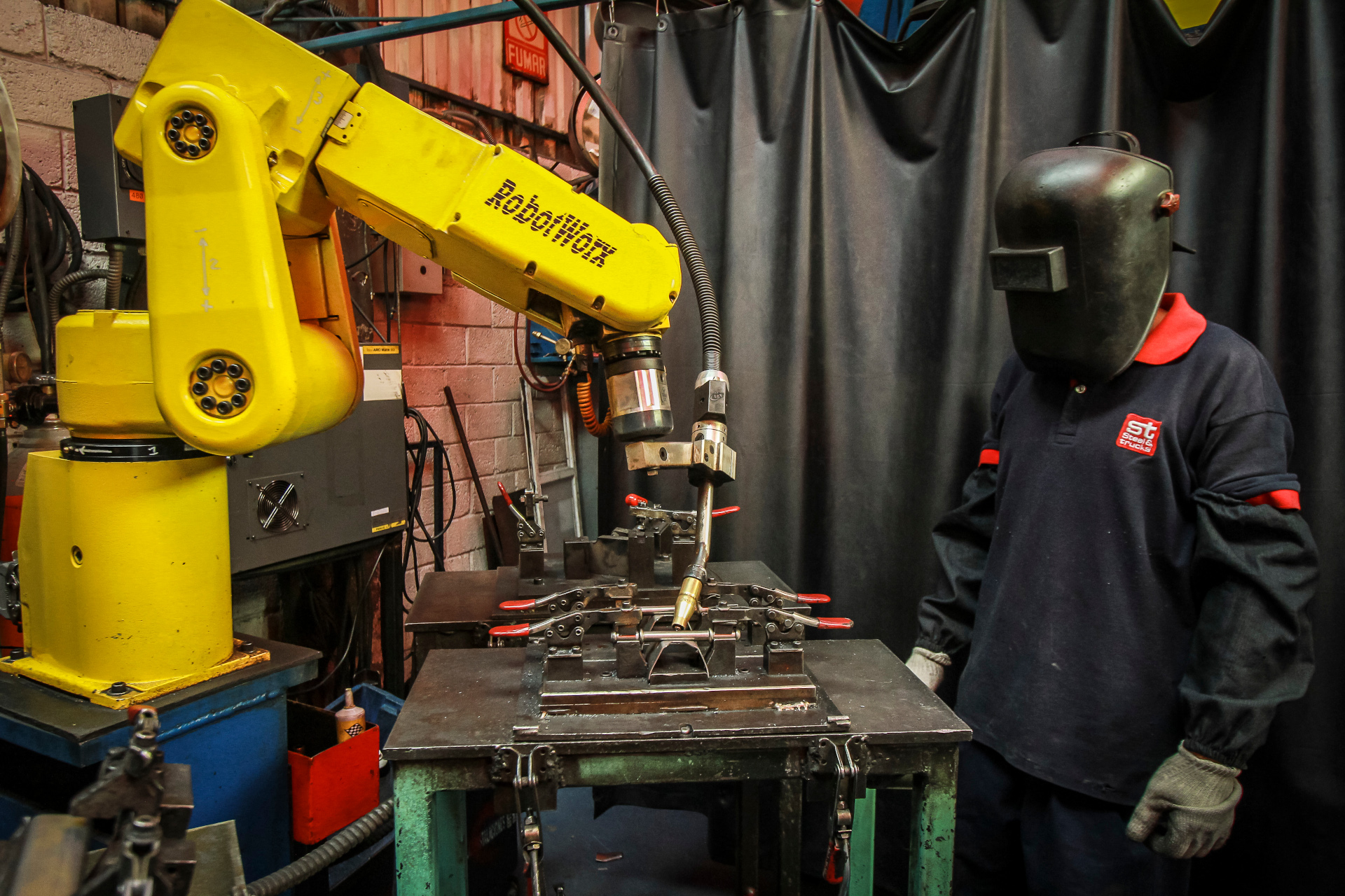 A welder wearing protective gear works in a workshop with visible sparks